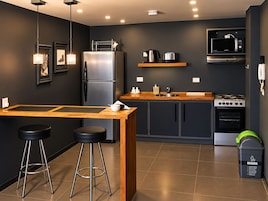 A modern kitchen with a central island, bar stools, a refrigerator, microwave, stove, and a trash bin.