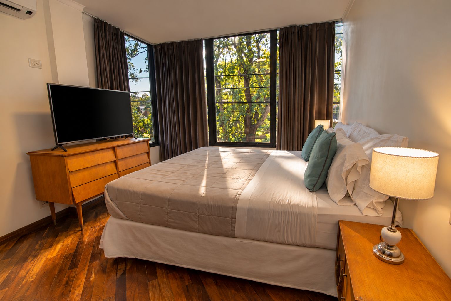 A hotel room with a large bed, a television on a wooden dresser, and a window with curtains.