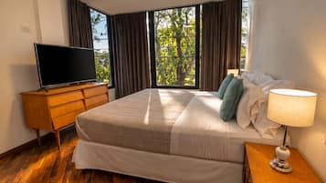 A hotel room with a large bed, a television on a wooden dresser, and a window with curtains.