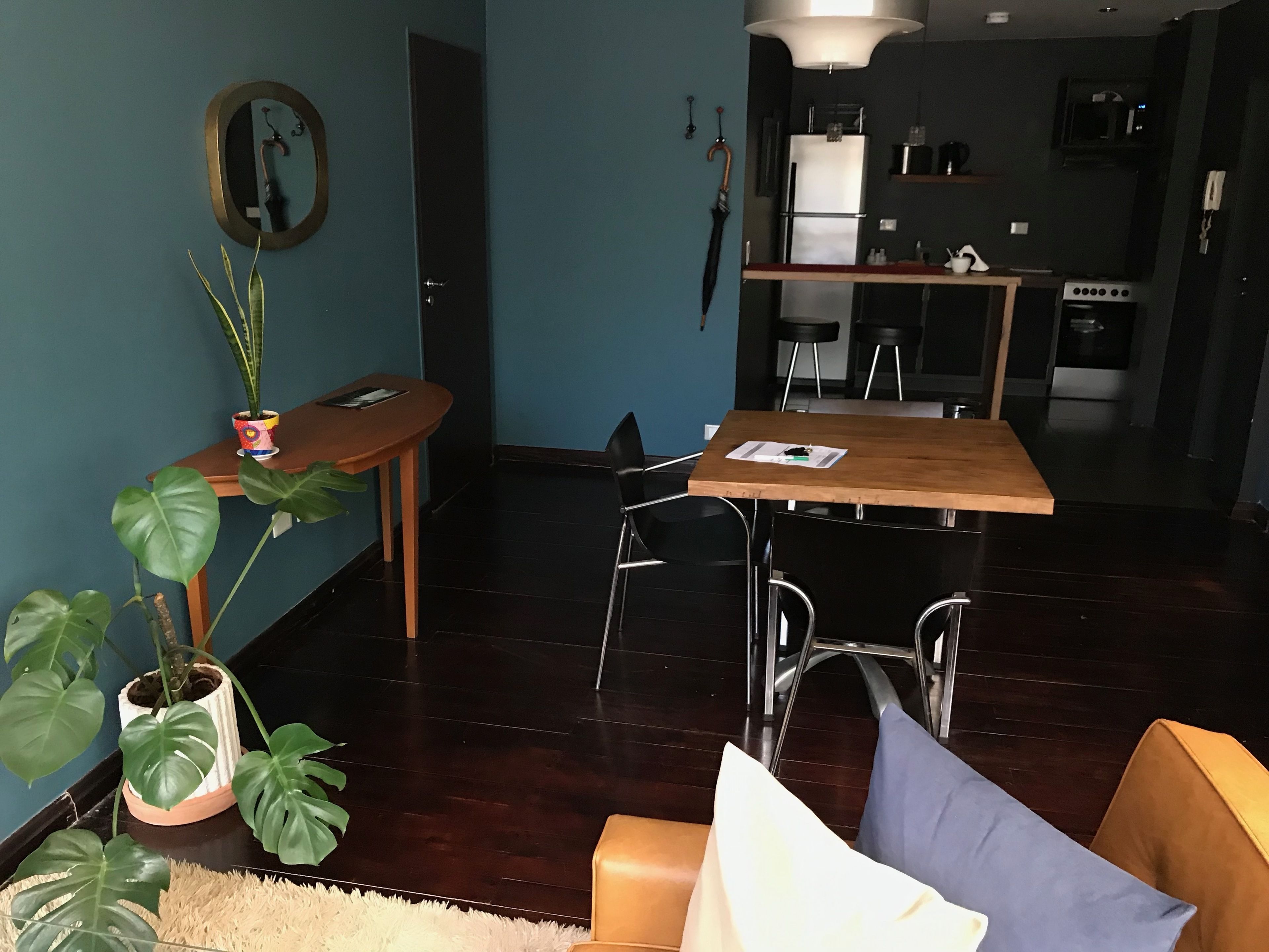 Un salon moderne avec une table à manger en bois, un canapé et une table basse. On aperçoit à l’arrière-plan un coin cuisine équipé d’un réfrigérateur et d’un four à micro-ondes.