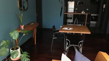Un salon moderne avec une table à manger en bois, un canapé et une table basse. On aperçoit à l’arrière-plan un coin cuisine équipé d’un réfrigérateur et d’un four à micro-ondes.