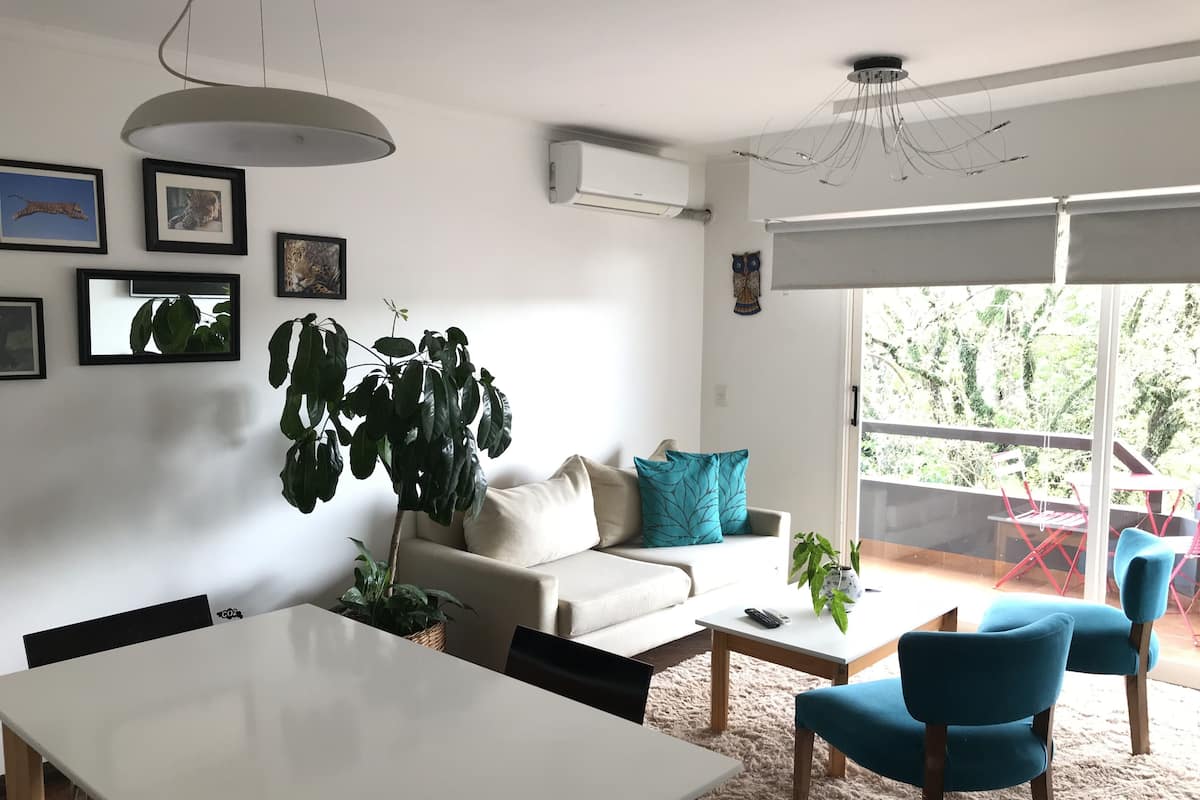 Un salon moderne comprenant un canapé, une table basse et des fauteuils, une table à manger et une grande plante.