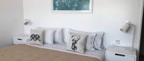 Un dormitorio ordenado con una cama grande, dos mesitas de noche con lámparas y una obra de arte enmarcada en la pared.
