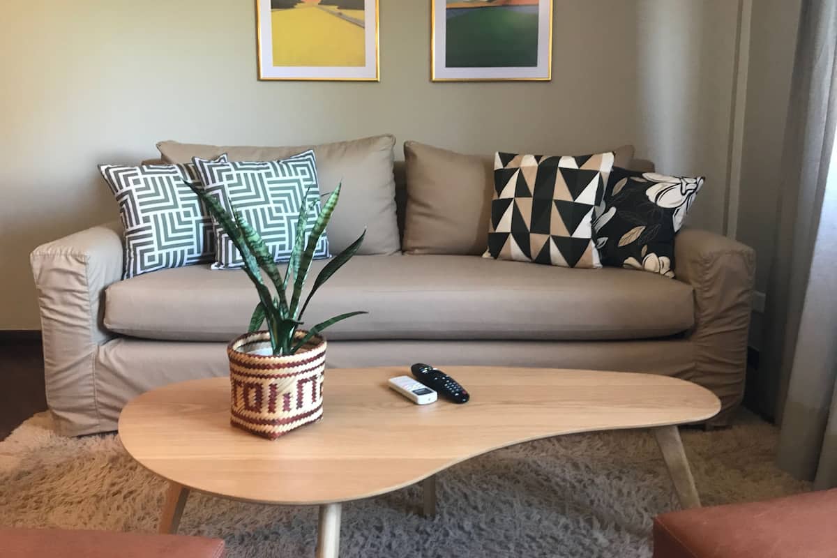 Un salon avec un canapé beige, des coussins à motifs, une table basse en bois ornée d’une plante, et deux œuvres d’art encadrées accrochées au mur.