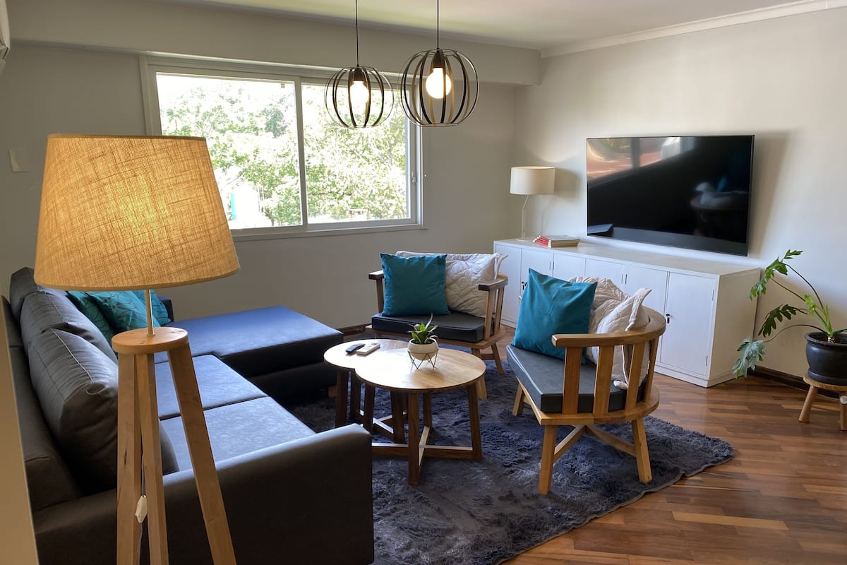 Un salon moderne avec un canapé, des fauteuils, une table basse, un téléviseur et une grande fenêtre.