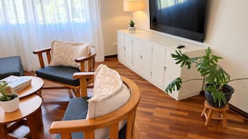 Una sala de estar con sofá, sillas, televisor, aparador y planta en maceta.