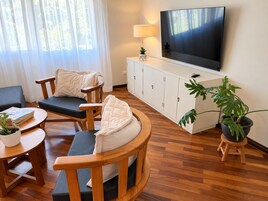 Una sala de estar con sofá, sillas, televisor, aparador y planta en maceta.