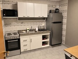 Una cocina con armarios blancos, un refrigerador de acero inoxidable, un microondas, una estufa y un lavadero con escurreplatos.