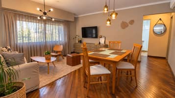 Una sala de estar con una mesa de comedor de madera, sillas, un sofá, un televisor y una chimenea.