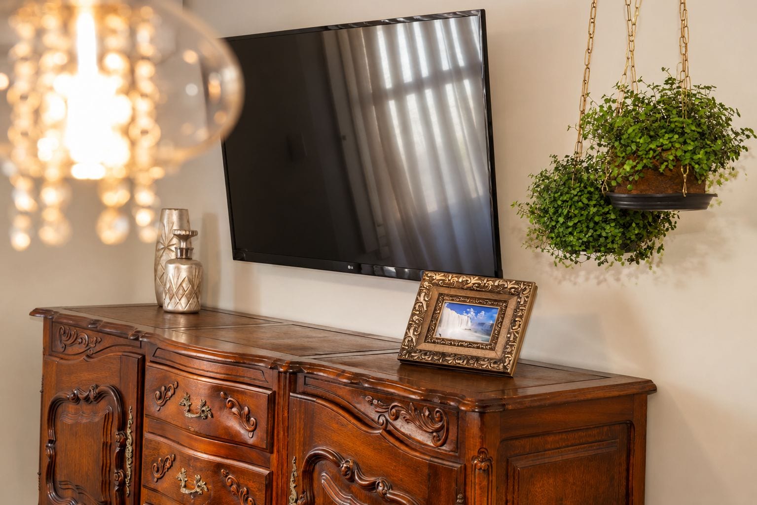 A wooden cabinet with drawers, a framed picture, a television, and a hanging plant.