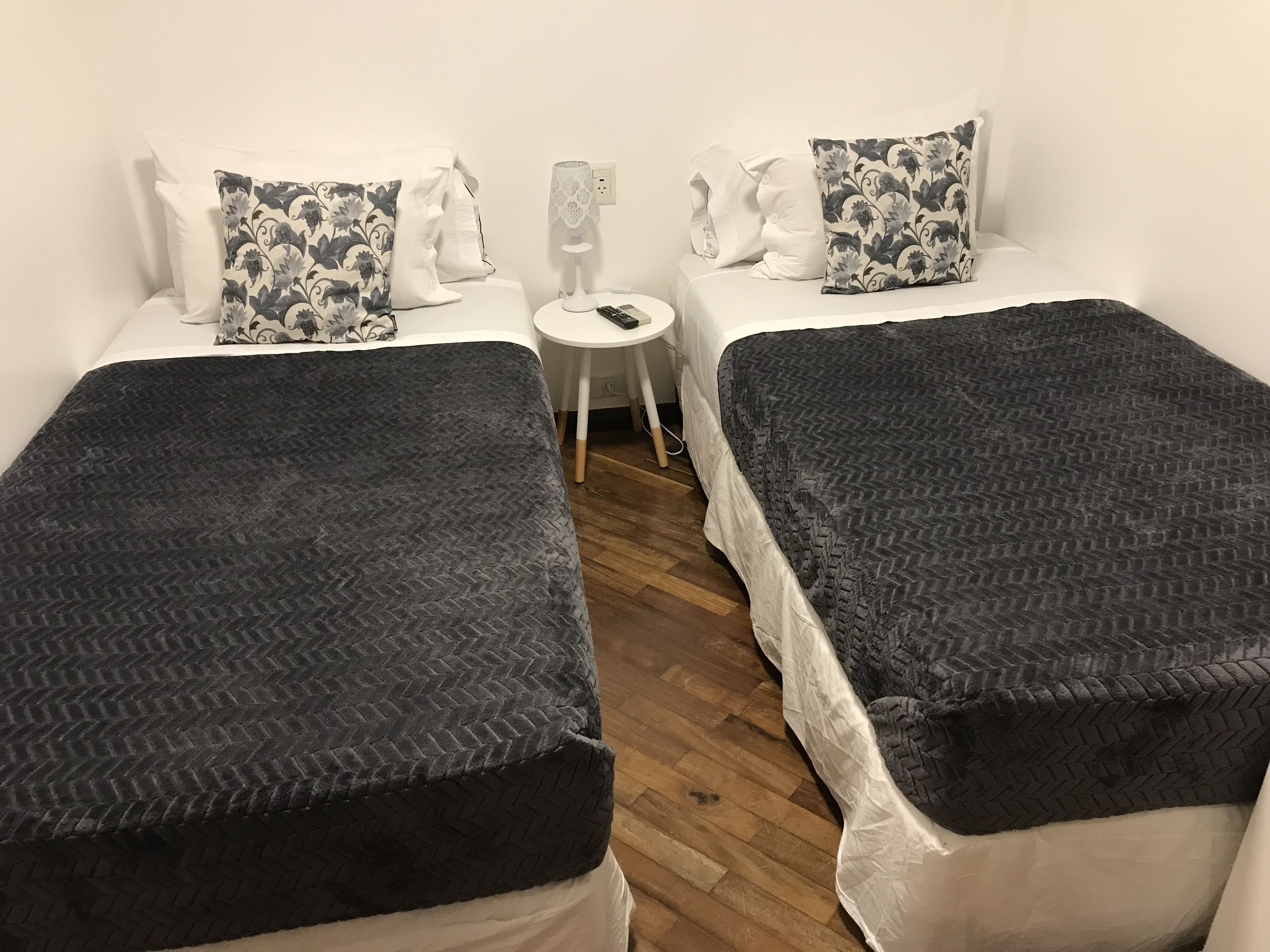 A room with two single beds, each with a dark patterned bedspread and white pillows. There is a small round table with a lamp between the beds.