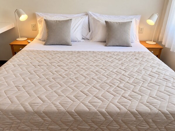 Una cama bien hecha con un cabecero acolchado, dos lámparas de noche y una mesita de madera.