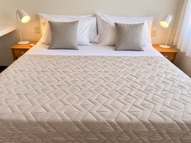Una cama bien hecha con un cabecero acolchado, dos lámparas de noche y una mesita de madera.