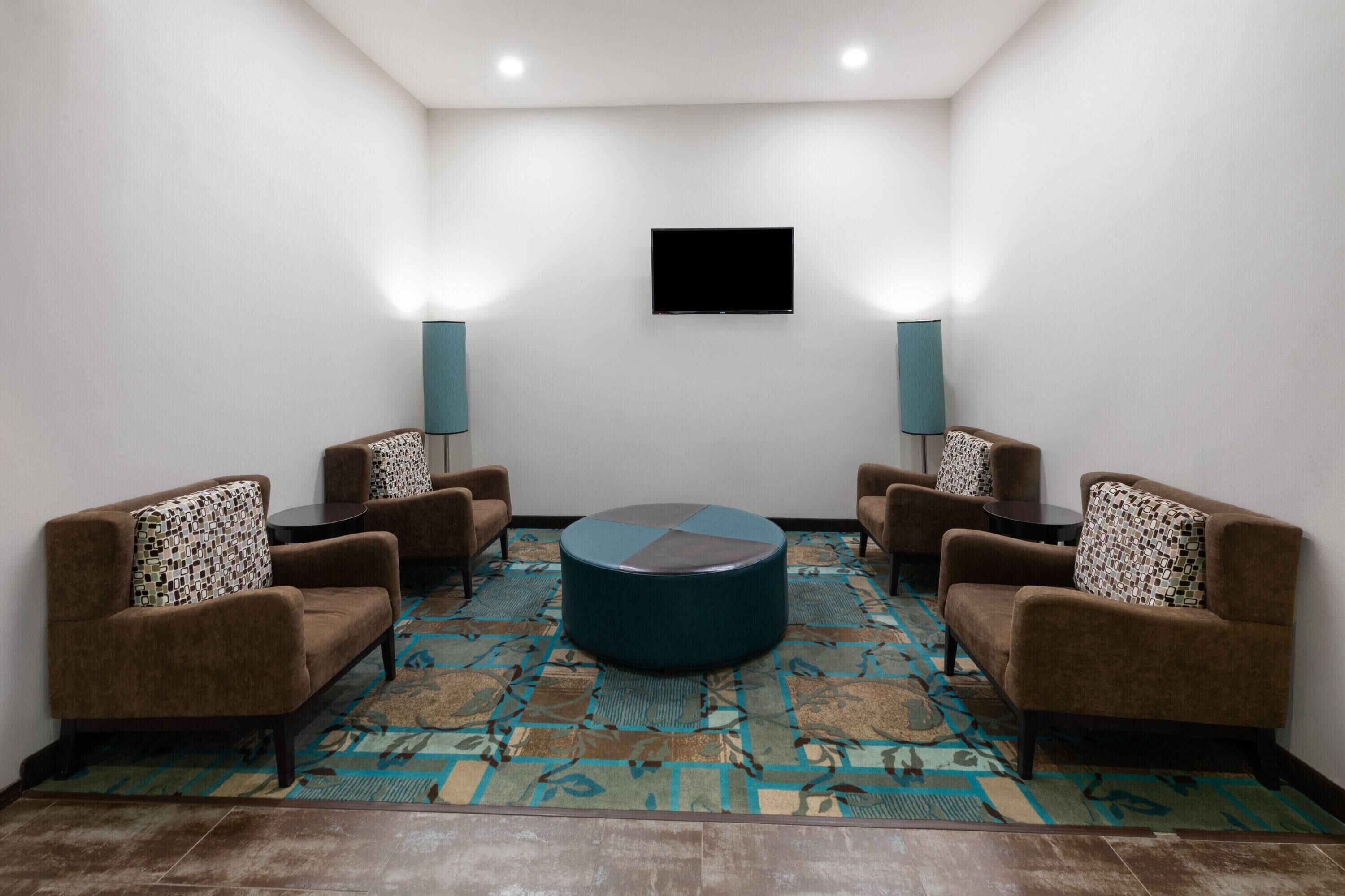 A conference room with a round table, four brown sofas, patterned floor, and two wall-mounted lamps.