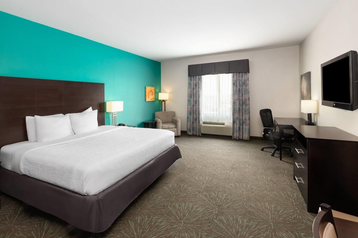 A hotel room with a large bed, a desk, a chair, a TV, and a window with curtains.