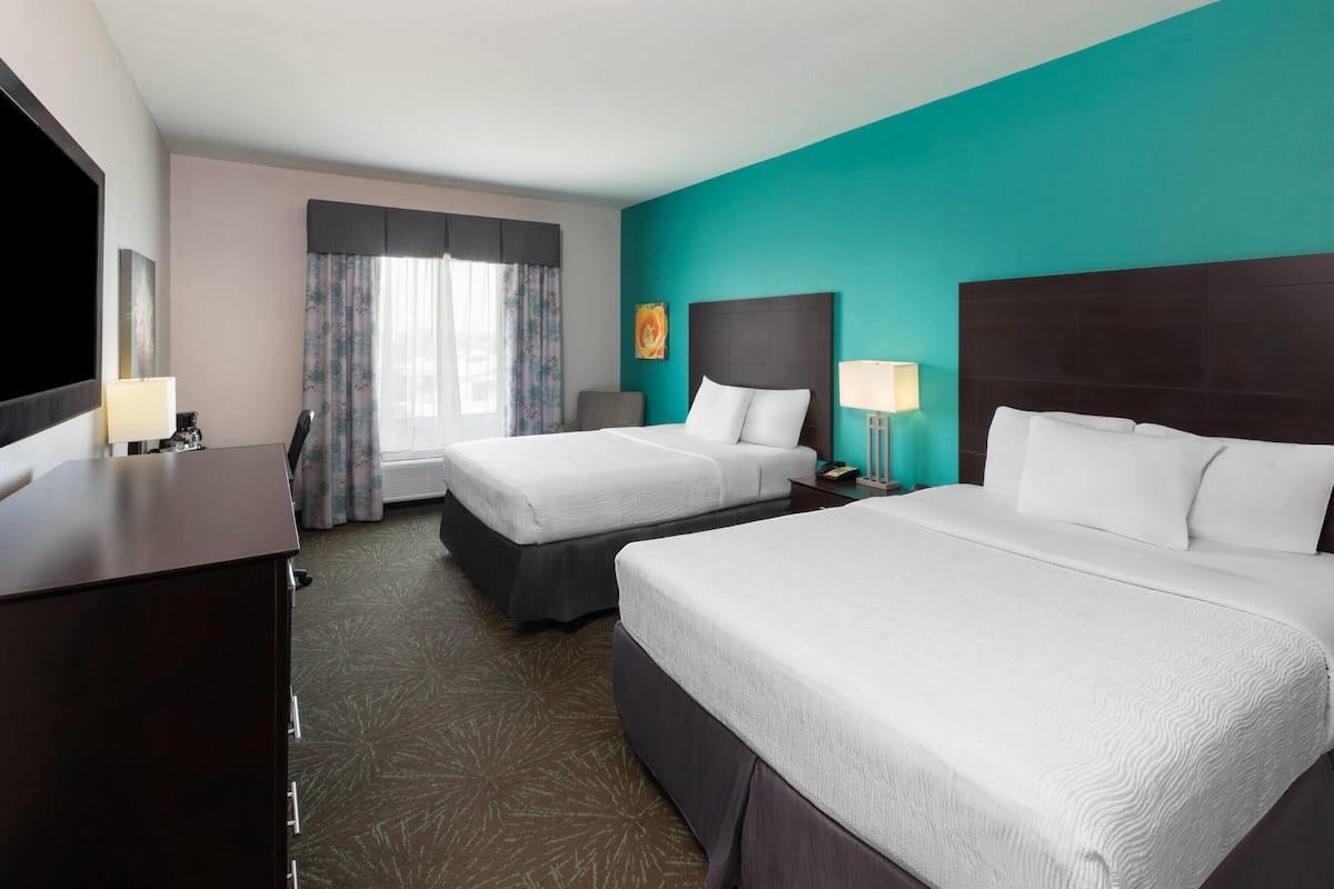 A hotel room with two beds, a desk, a TV, and a window with curtains.