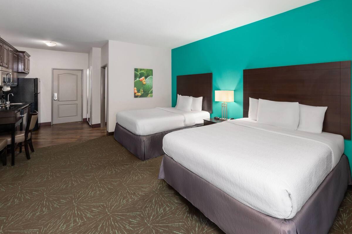A hotel room with two beds, a desk, and a kitchenette.