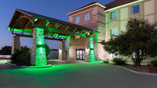 A hotel entrance with a covered walkway and stone pillars, illuminated by green lighting.