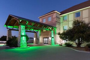 Een hotel ingang met een overdekte gang en stenen pilaren, verlicht met groen licht.