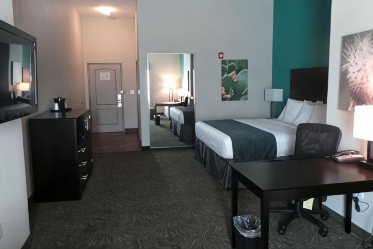 A hotel room with a bed, desk, chair, dresser, mirror, and a TV.