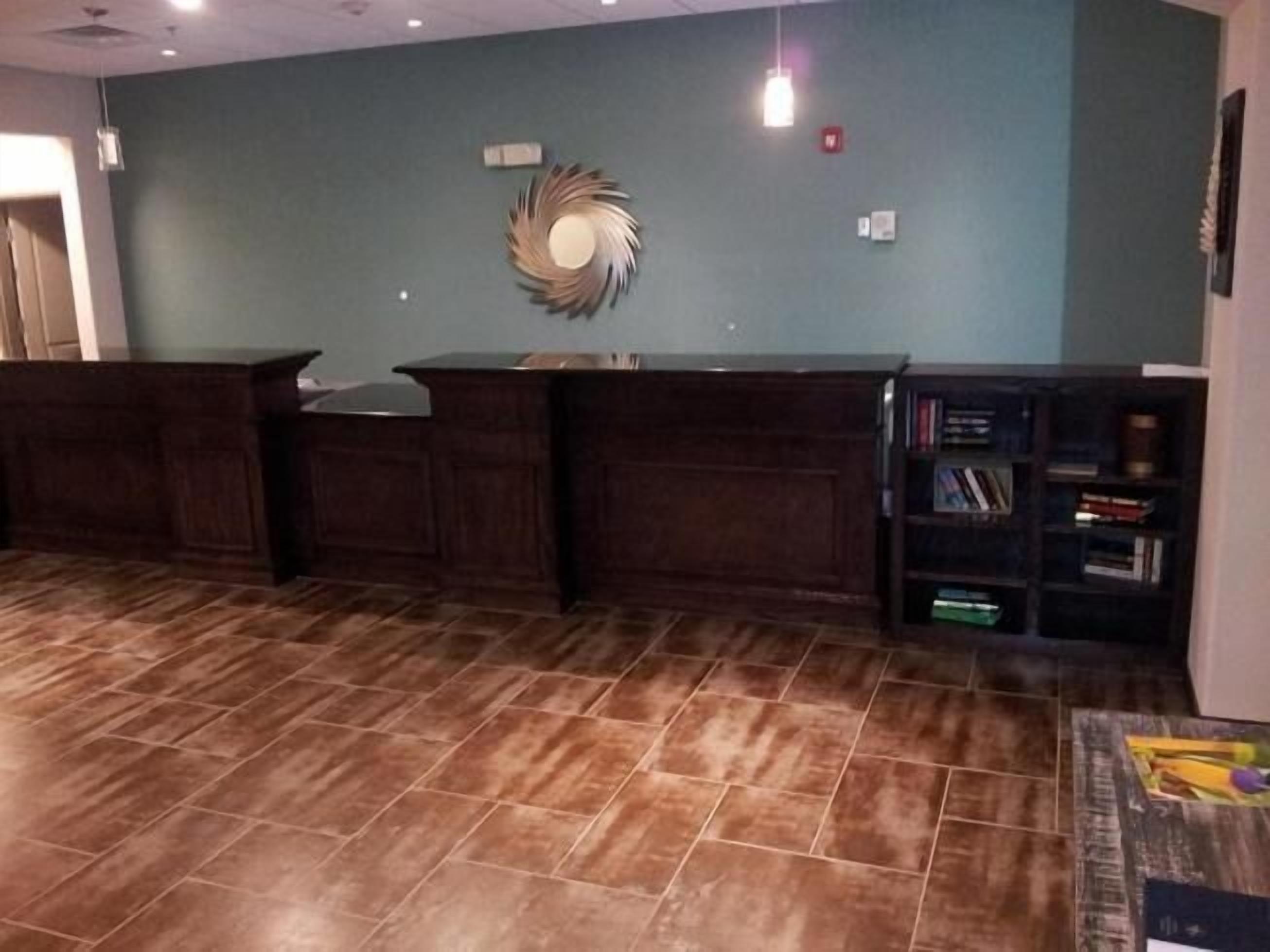 A reception area with a wooden reception desk, a wall-mounted decorative mirror, and a bookshelf with books.