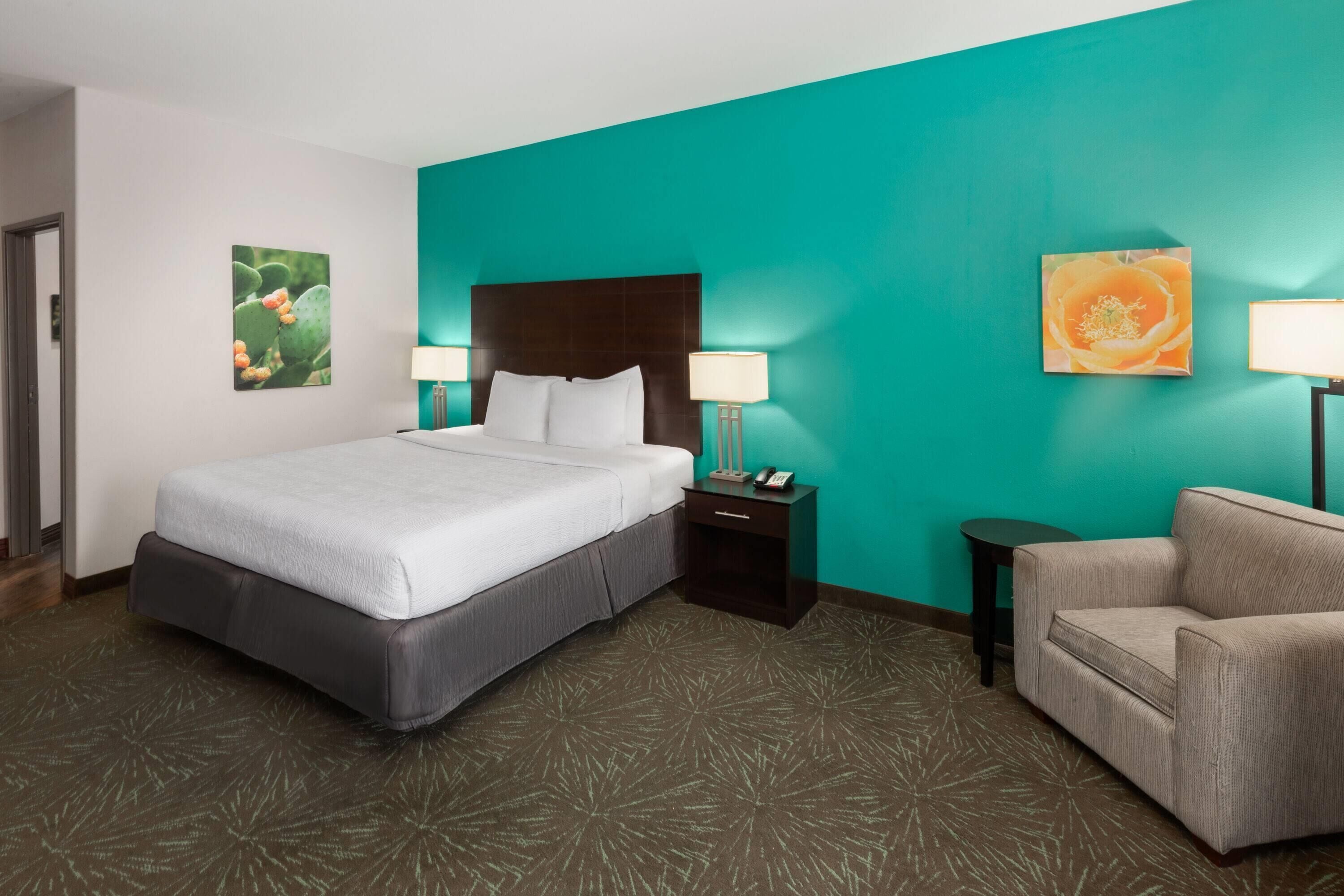 A hotel room with a large bed, a nightstand with a lamp, a chair, and artwork on the walls.