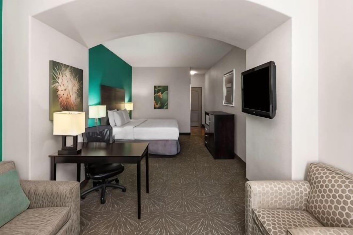 A hotel room with a bed, desk, chair, TV, and a couch.
