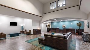A spacious lobby with a high ceiling, a reception desk, seating area, and a large window.