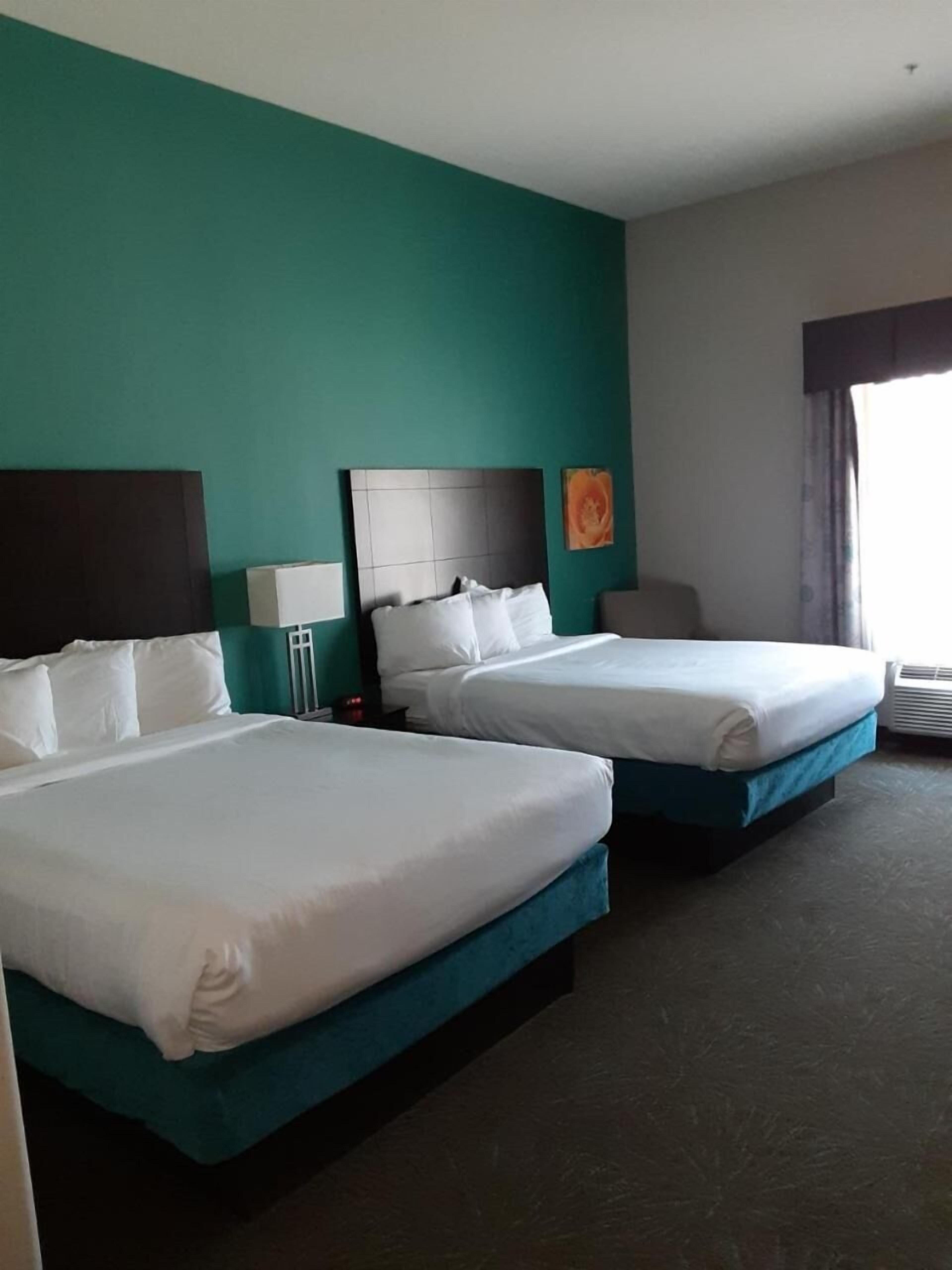 A hotel room with two beds, teal walls, and a large window with curtains.