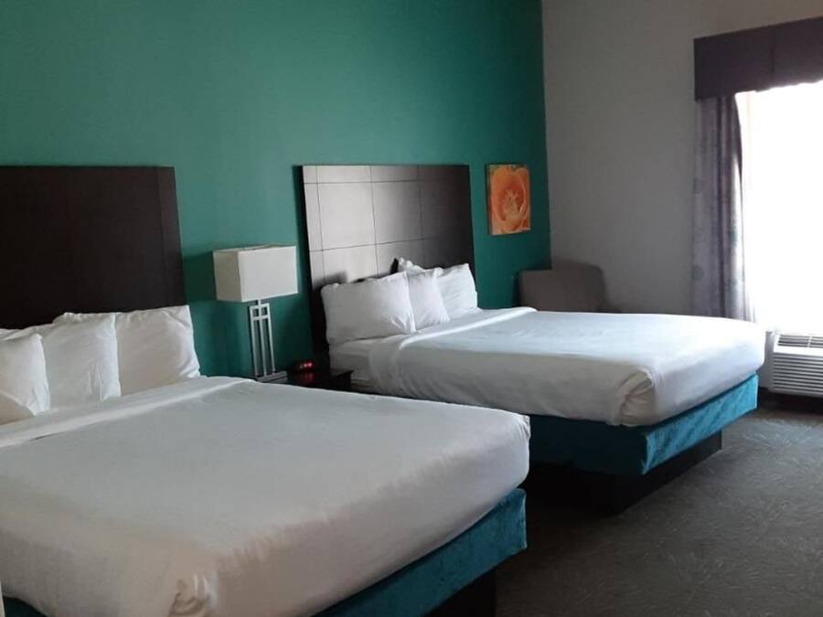 A hotel room with two beds, teal walls, and a large window with curtains.