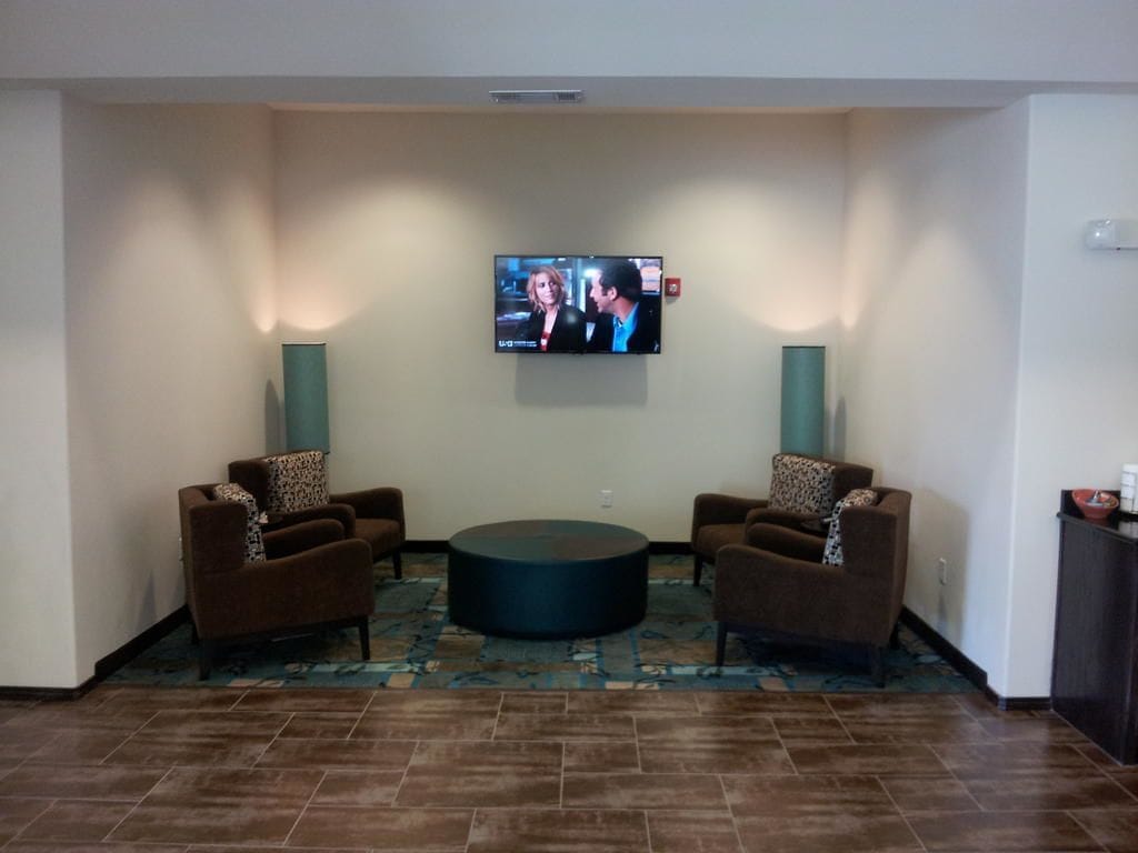 A lobby with two sofas facing a round coffee table, a flat-screen TV mounted on the wall, and a patterned rug on the floor.
