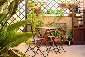 An outdoor patio with a table and chairs, surrounded by potted plants and a bamboo fence. - Il Lapino (Palermo)