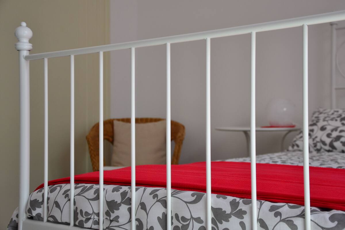 A white metal bed frame with a red bedspread and grey floral bedding.