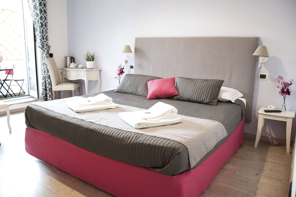 A neatly arranged bedroom with a large bed, bedside tables, a desk, and a chair.