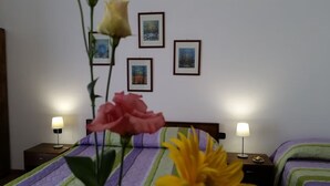 A hotel room with a bed, two bedside tables with lamps, a wall with framed pictures, and a flower in the foreground. - B&B Il Borgo (Scilla)