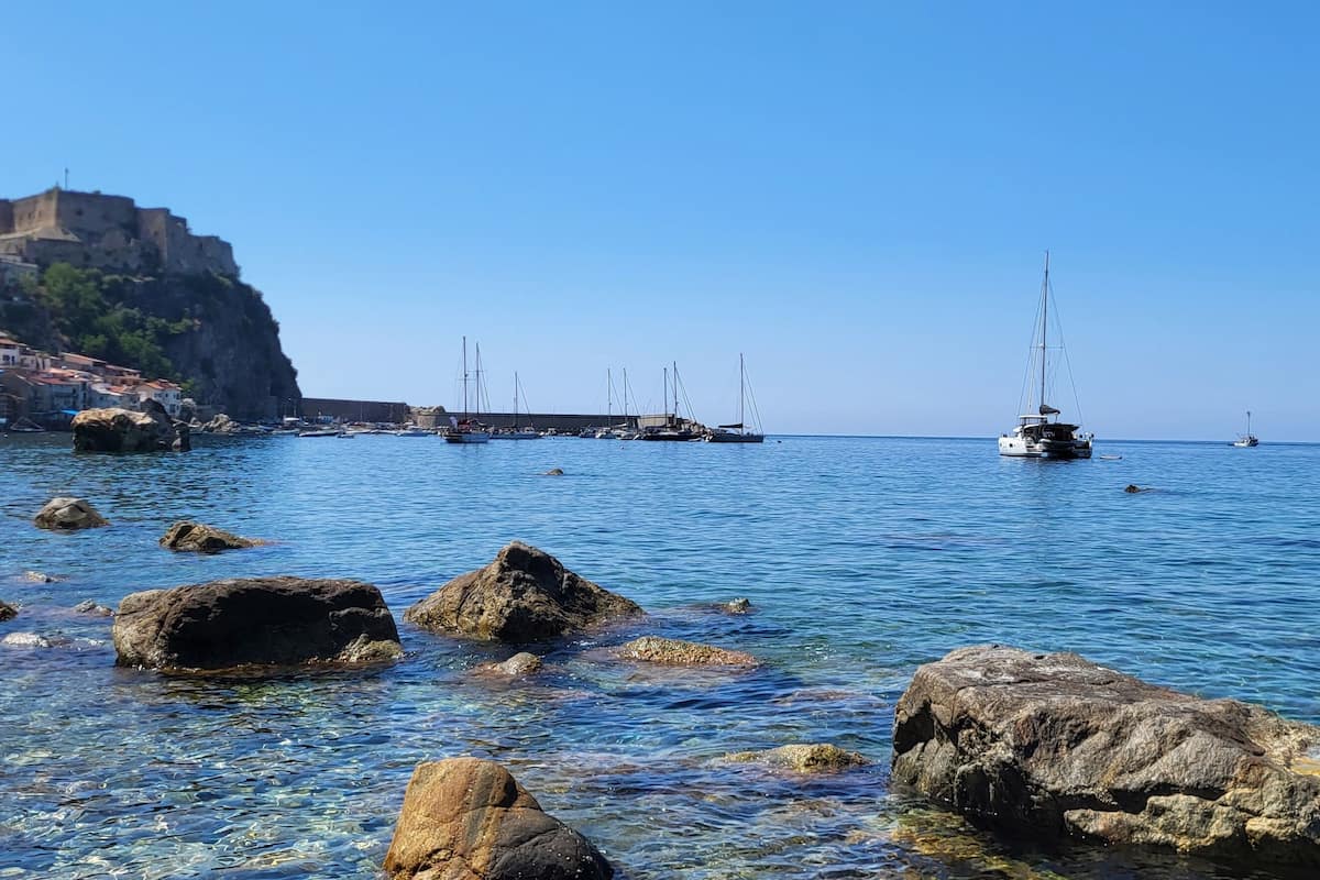 A coastal scene with clear waters, rocks, and a distant castle on a hill.