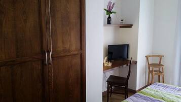 Ein Zimmer mit Holzschrank, Schreibtisch mit Computer, Stuhl und Bett mit grün-lilarer Steude.