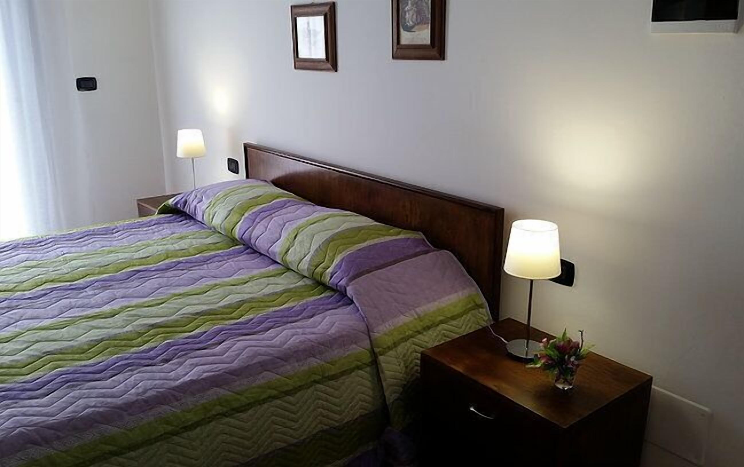 Una cama bien hecha con una colcha a rayas, una mesita de noche con una lámpara y dos cuadros en la pared.