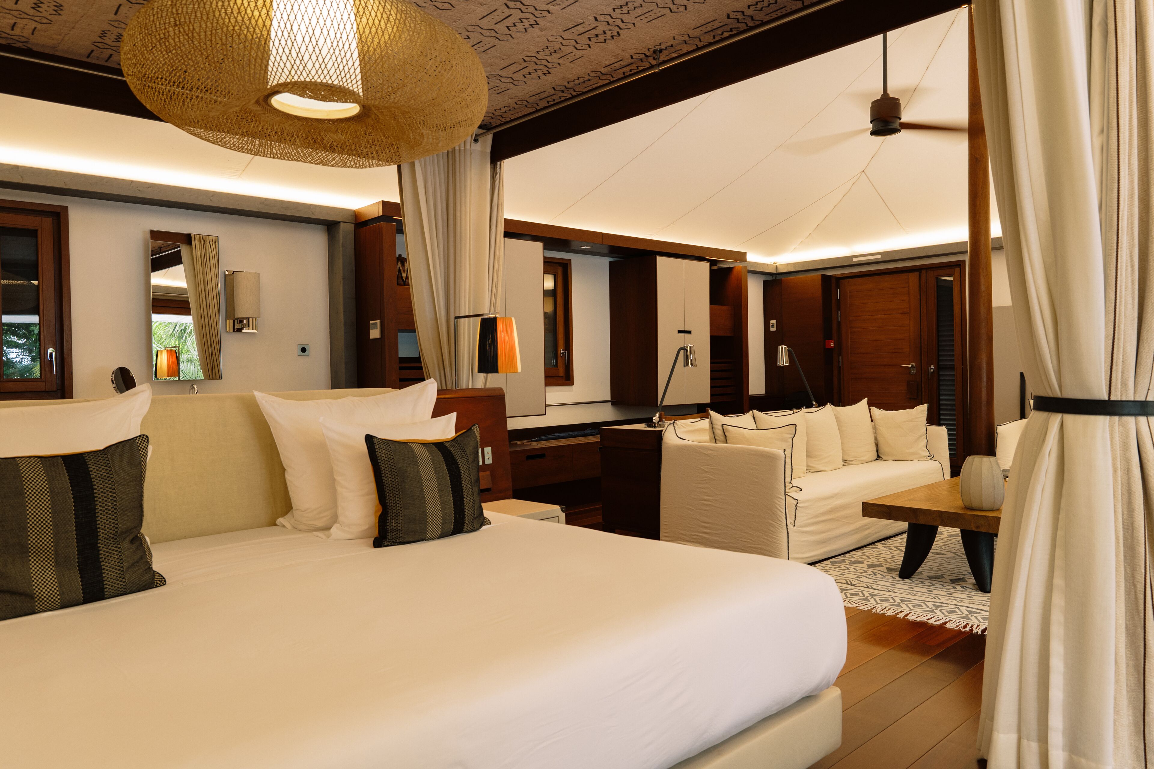 A spacious hotel room with a large bed, a sitting area with a sofa, a wooden desk, and a large mirror.