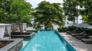 A swimming pool with a wooden deck, lounge chairs, and a tree in the background. - Sundy Praia – Principe Collection (Príncipe Island)