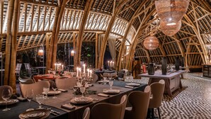 An indoor dining area with bamboo ceiling and walls, tables set with candles, and a bar area. - Sundy Praia – Principe Collection (Príncipe Island)