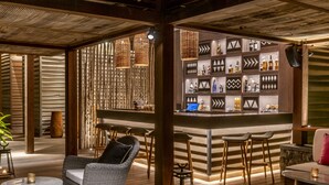 A bar area with wicker furniture, a wooden bar counter, and shelves with bottles. - Sundy Praia – Principe Collection (Príncipe Island)