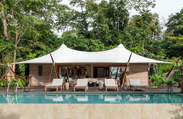 A poolside area with a covered seating area, lounge chairs, and a wooden deck. - Sundy Praia – Principe Collection (Príncipe Island)