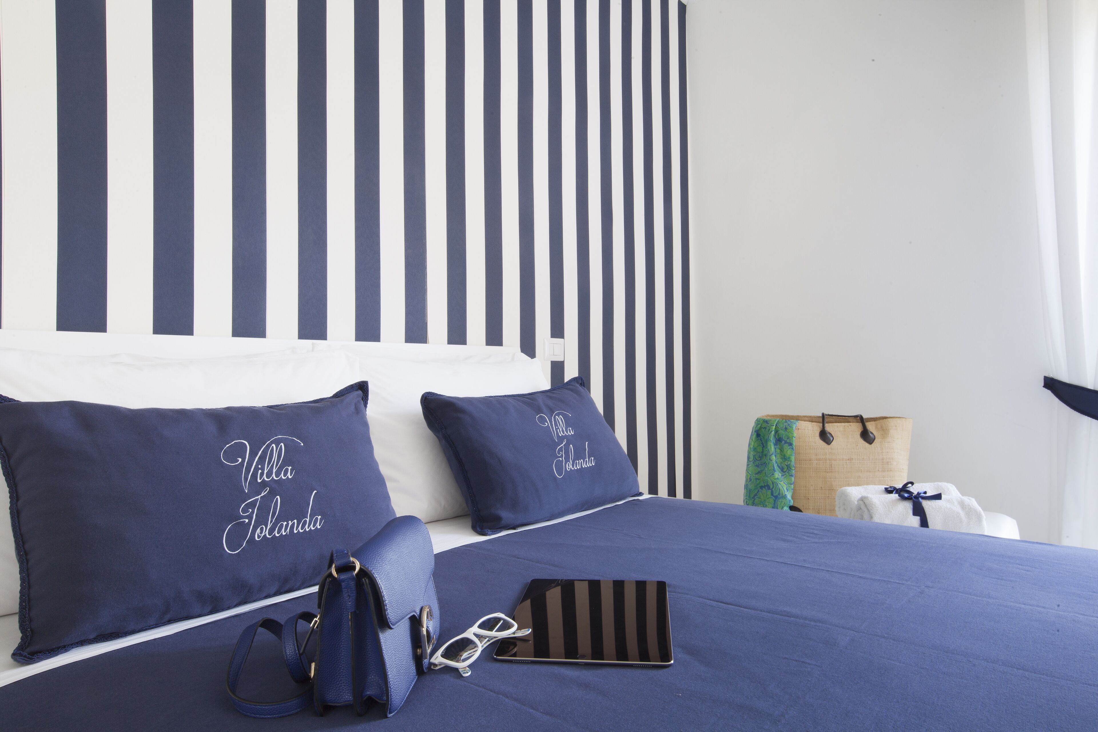 Ein ordentlich bezogenes Bett mit dunkelblauer Bettwäsche und Kissen, eine blaue Handtasche und ein Tablet auf dem Bett.