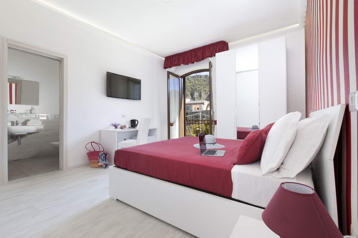 Un dormitorio moderno con cama, televisión, baño con lavamanos y vista a un balcón.