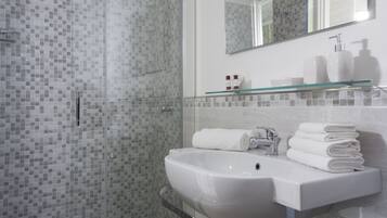 Un baño moderno con cabina de ducha de vidrio, un lavabo blanco con repisa de vidrio encima y un espejo sobre el lavabo.