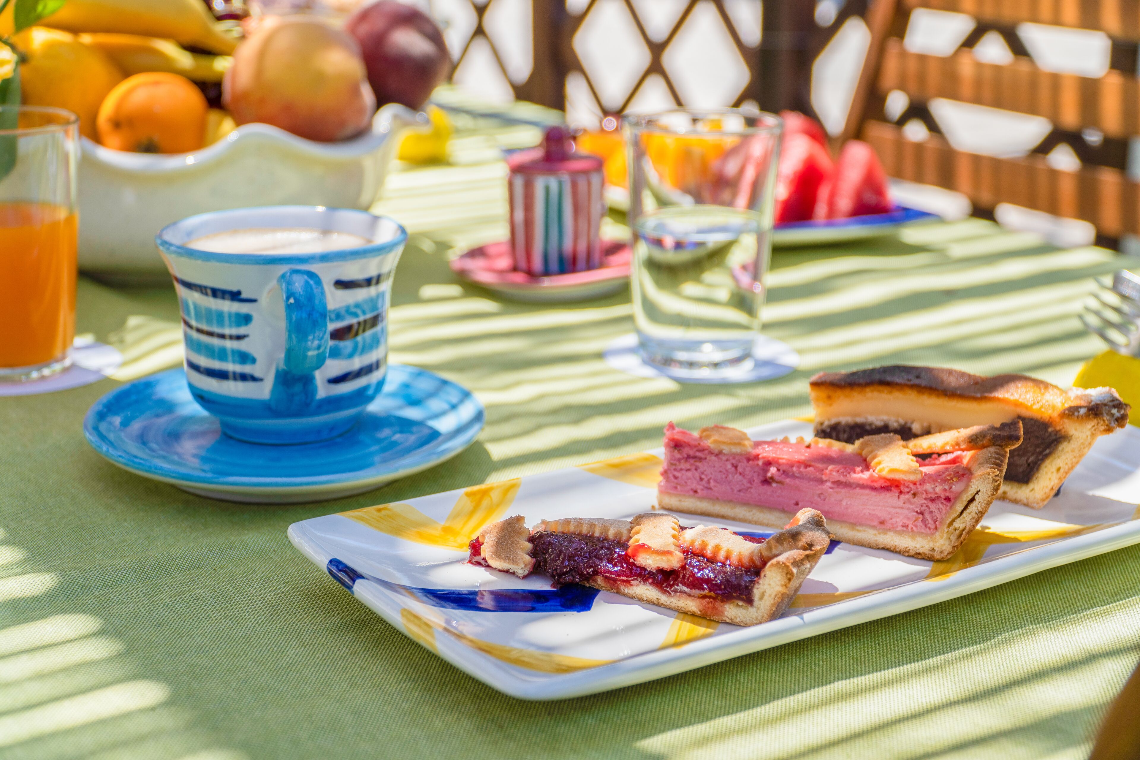 A breakfast setting with a plate of pastries, a jug of orange juice, and a cup on a table with a green tablecloth.
