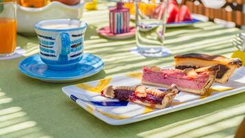 A breakfast setting with a plate of pastries, a jug of orange juice, and a cup on a table with a green tablecloth.