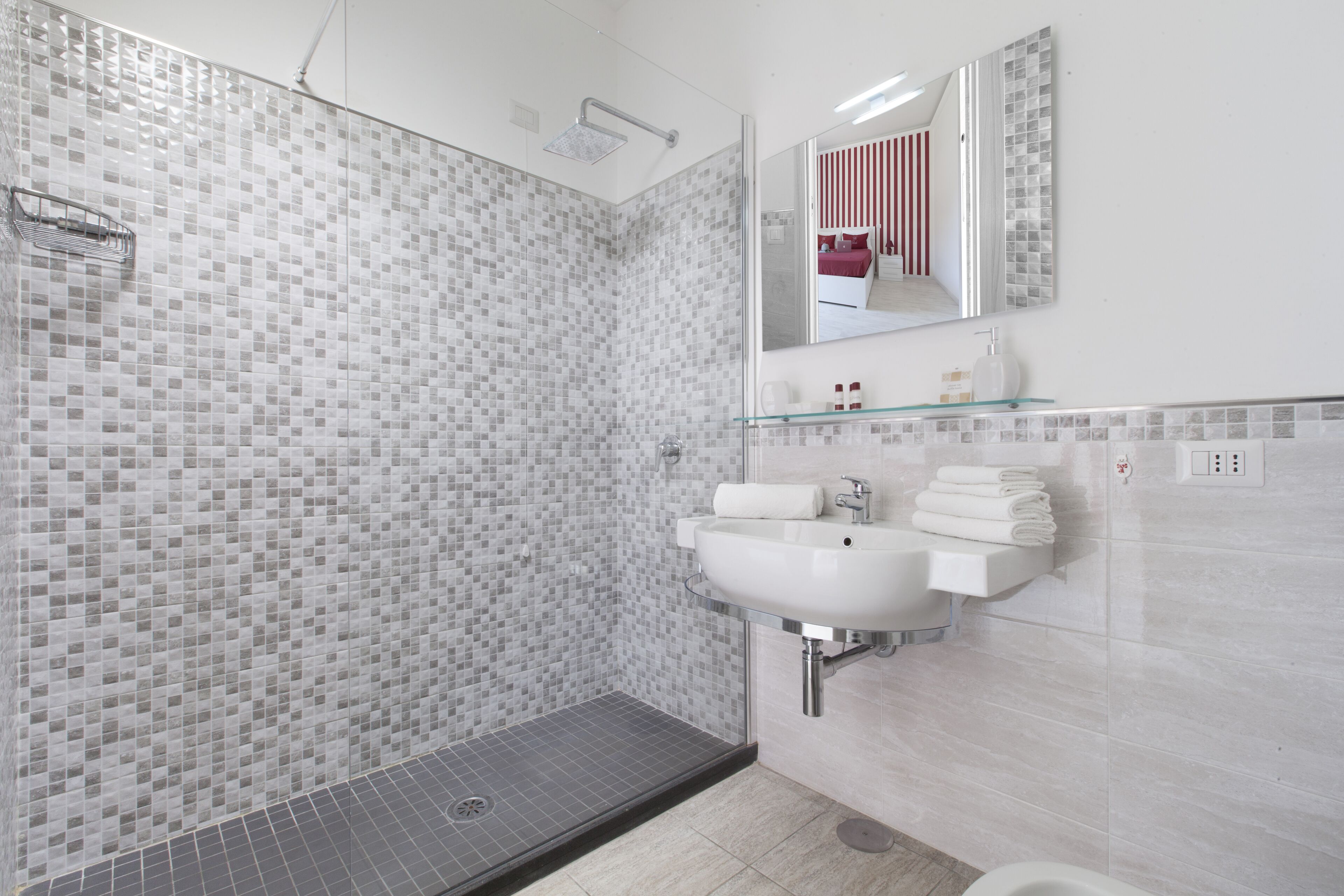 A modern bathroom with a glass shower enclosure, a white sink, and a glass shelf above the sink.