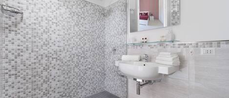 A modern bathroom with a glass shower enclosure, a white sink, and a glass shelf above the sink.